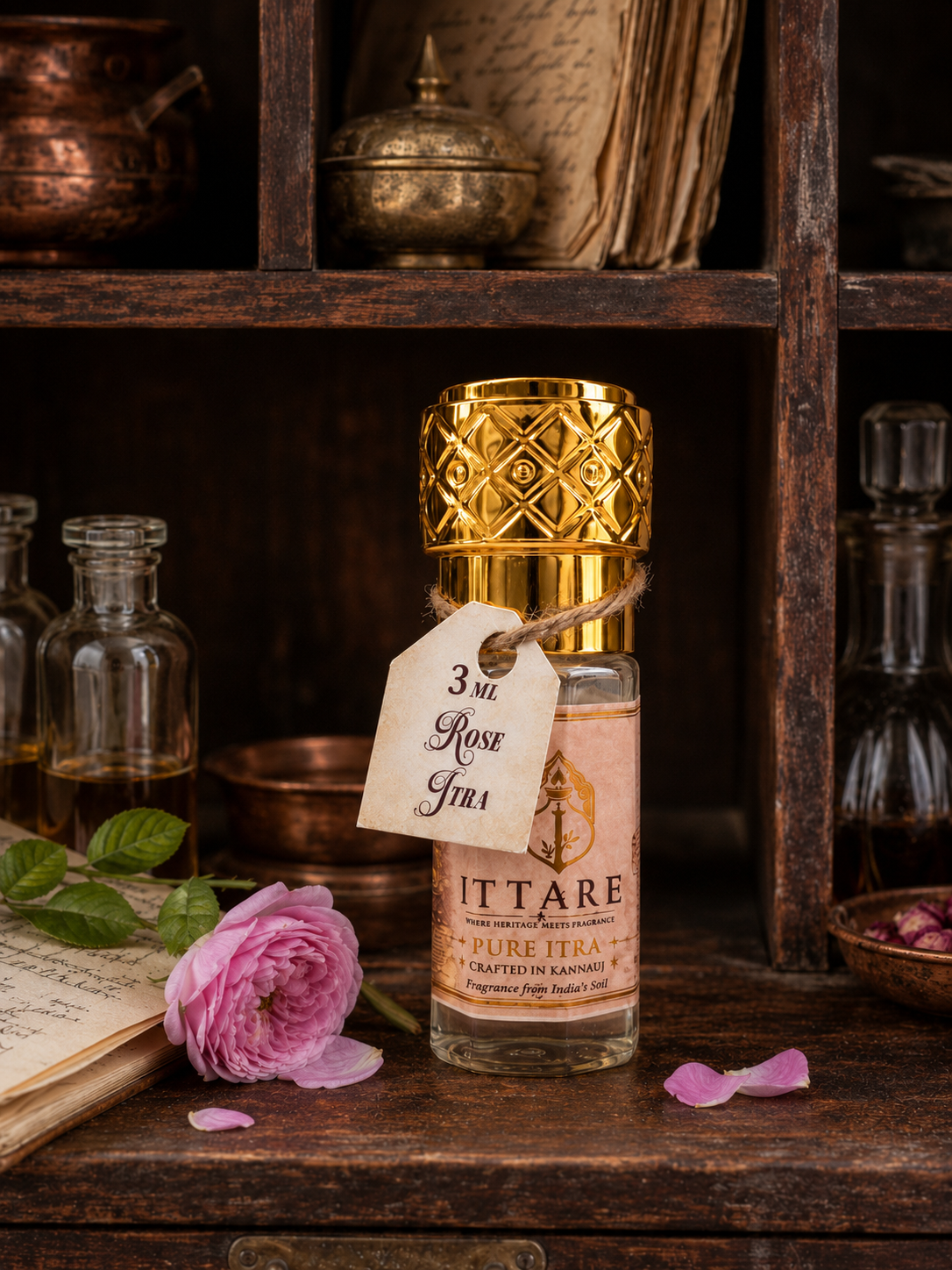 Rose Itra bottle with a gold cap beside a pink rose